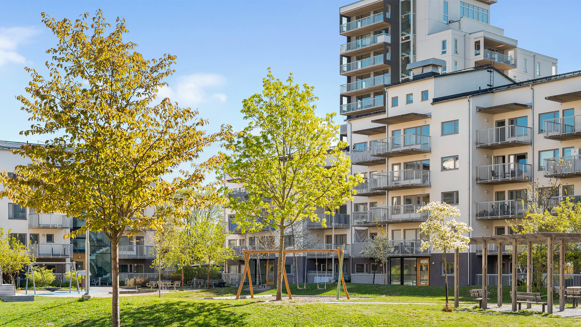 Innergård med gungor och sittplatser, flerbostadshus i flera våningar i bakgrunden