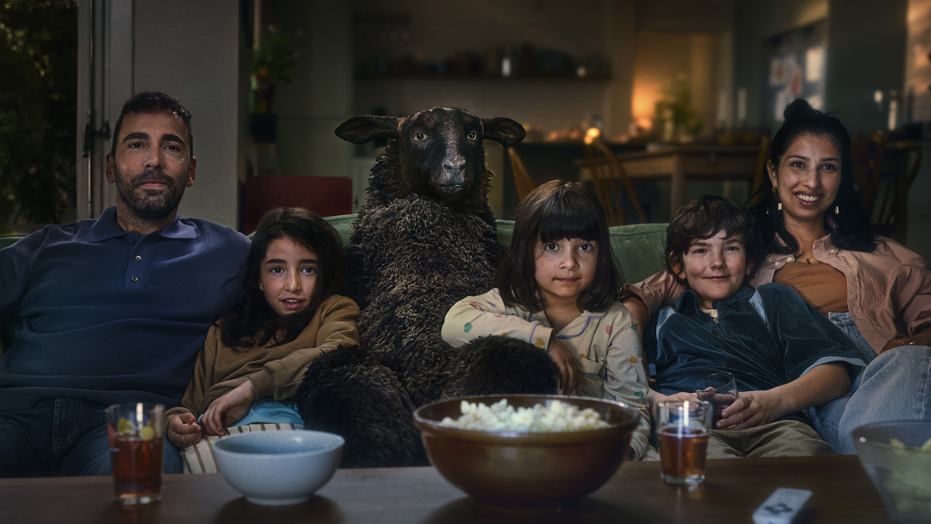 Fem personer som tittar på tv med ett svart får i soffan