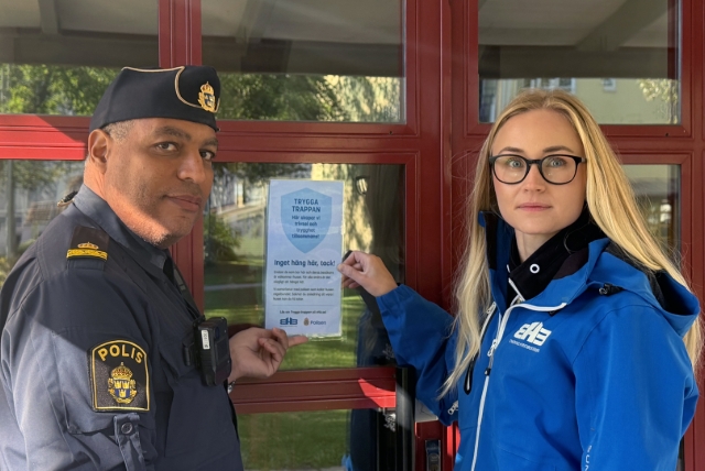 En polis och medarbetare från EHB framför en entré med en lapp uppsatt