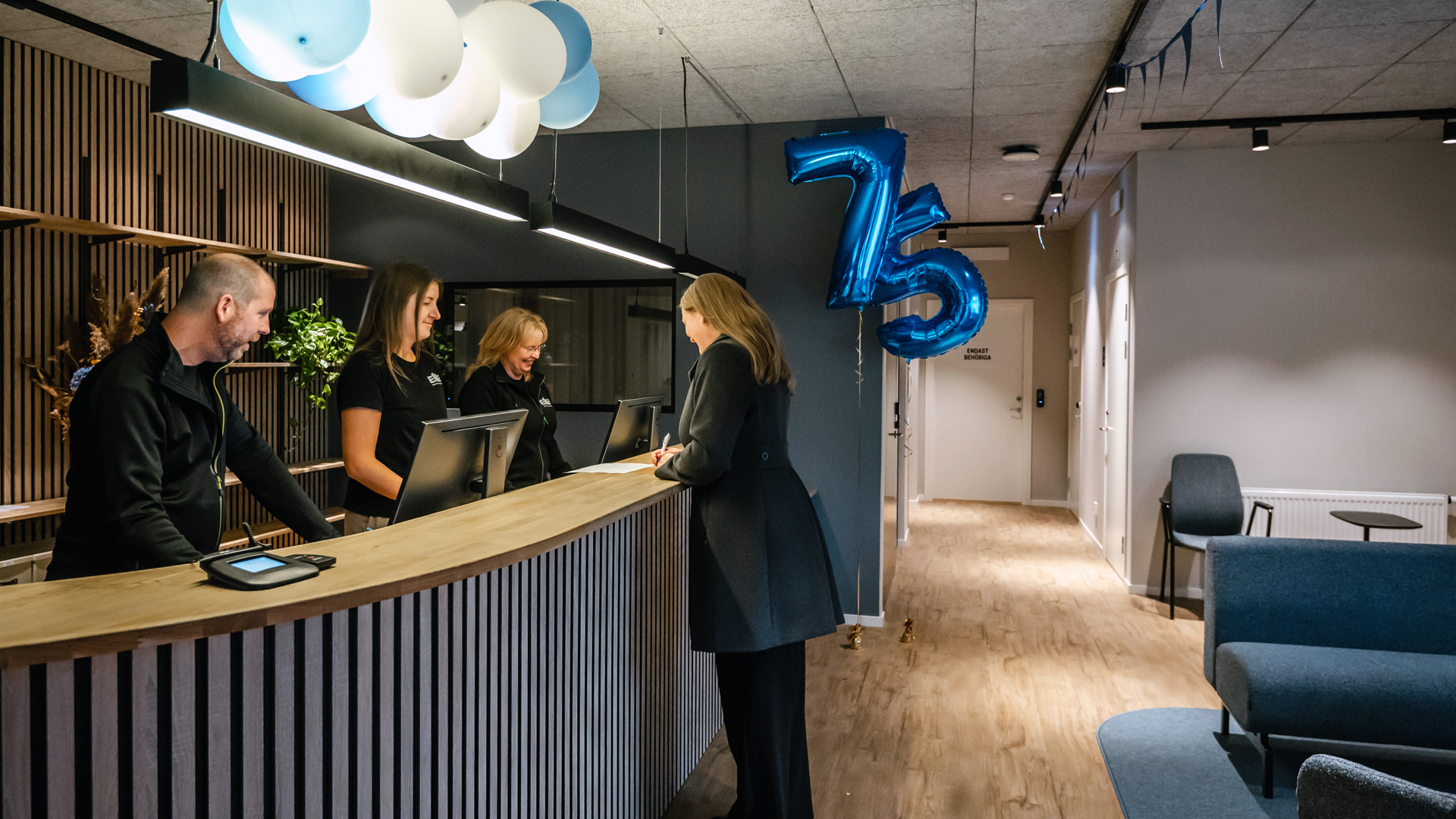 Tre medarbetare bakom en receptionsdisk som hjälper en besökare