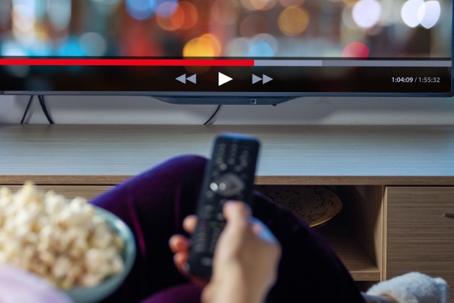 En kvinna sitter med en skål popcorn och håller i fjärrkontrollen till tv:n